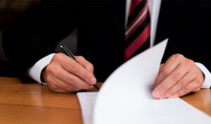 Abogado corporativo en traje firmando un documento oficial de reclamación de seguros sobre un escritorio de madera