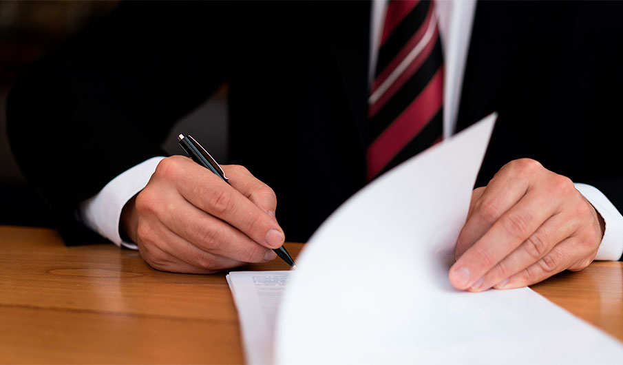 Abogado corporativo en traje firmando un documento oficial de reclamación de seguros sobre un escritorio de madera
